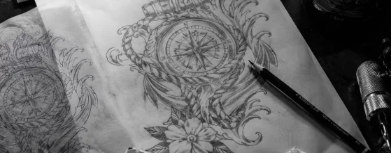 Boceto a lápiz de tatuaje personalizado sobre mesa de tatuador con material de diseño.